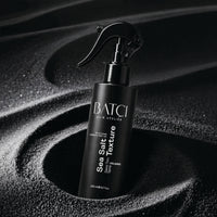 Batci Sea Salt spray placed on a black textured sand.